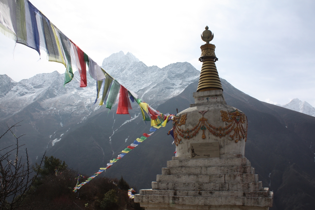 Stupa with prayer flags against a mountain backdrop.