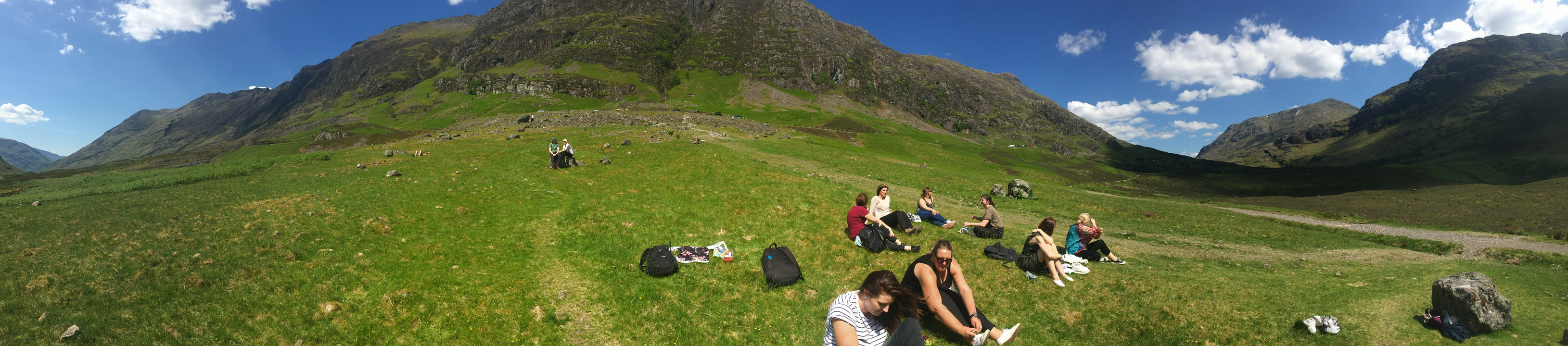 People sitting on grass with mountains in the background.