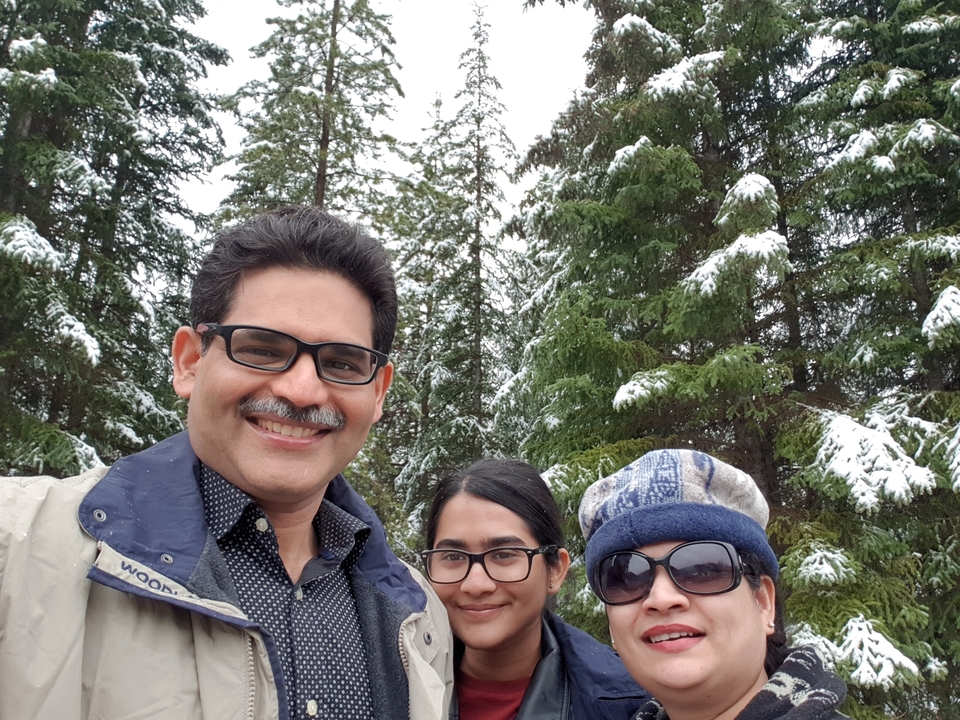 Famille posant dans une forêt enneigée avec des arbres à feuilles persistantes.