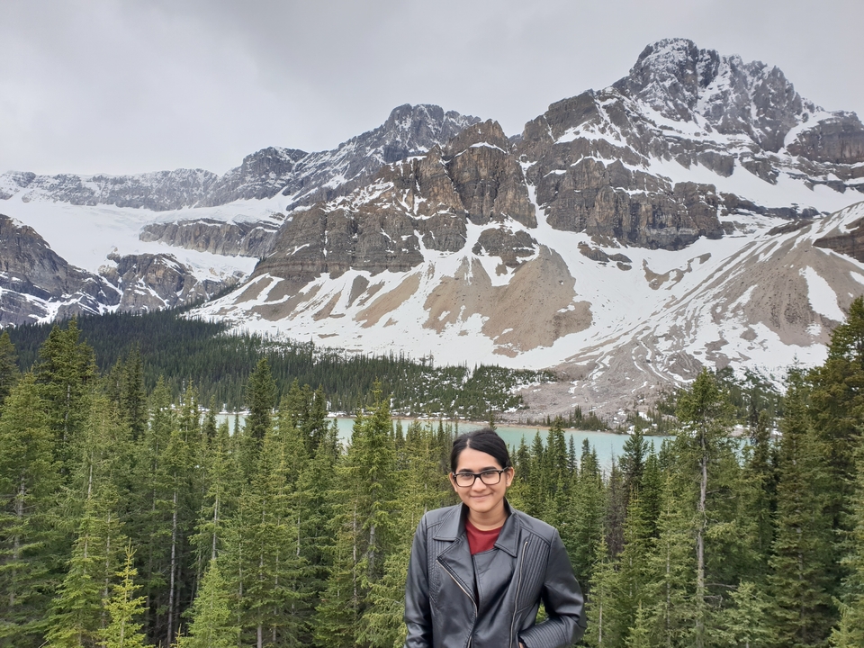 Femme posant avec un lac de montagne et des sommets enneigés en toile de fond.