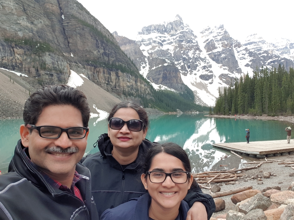 Famille posant au bord d'un lac de montagne avec des sommets enneigés.