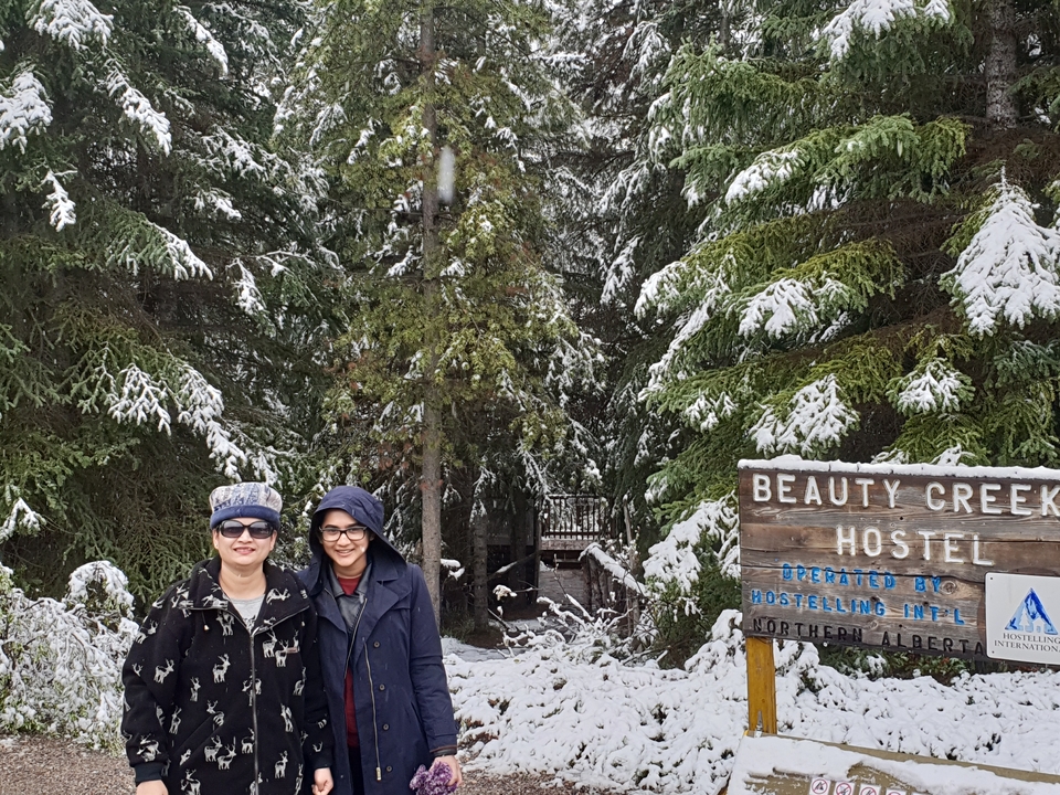 Deux individus posant près d'un panneau d'auberge dans une forêt enneigée.