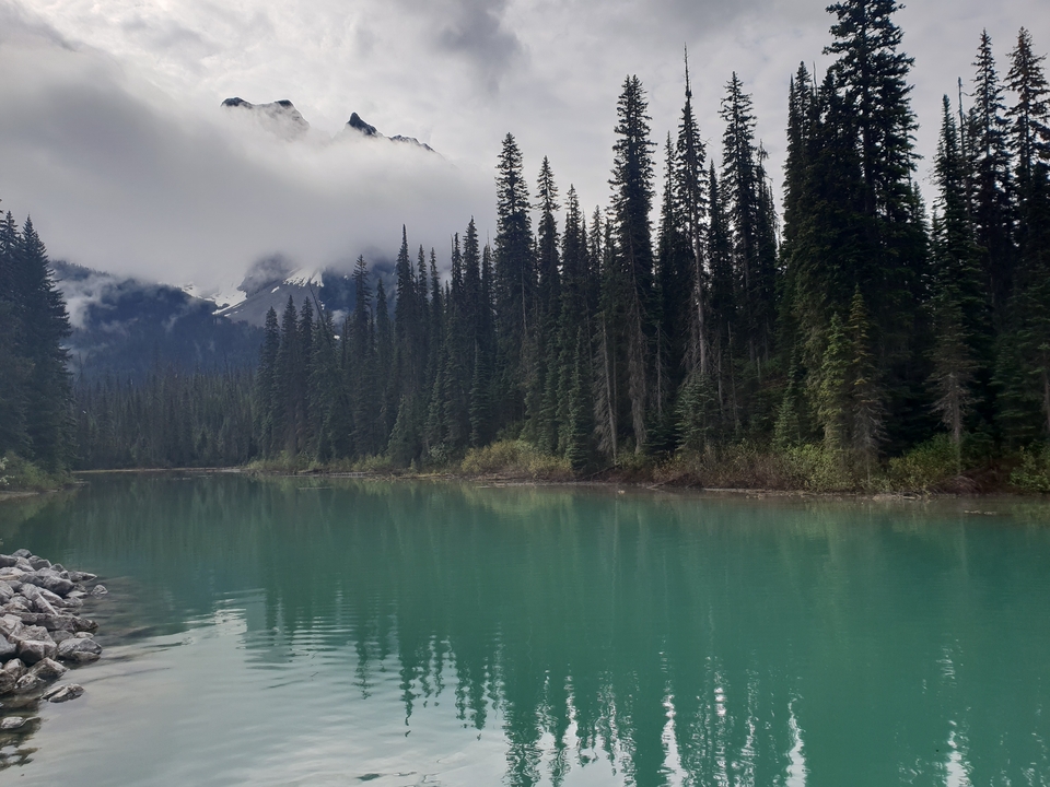 Calm lake surrounded by trees with mountains in the background.