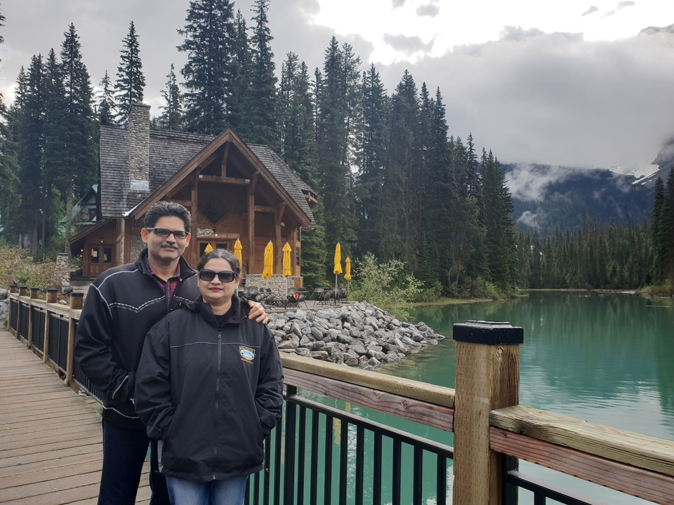 Couple posant sur une promenade avec un lac et des cabanes en arrière-plan.