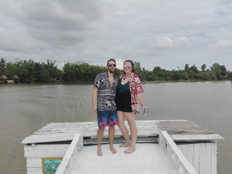 Two people posing on a pier with greenery in the background.