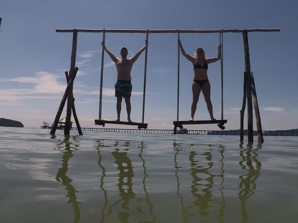 Two people playing on swings over water.