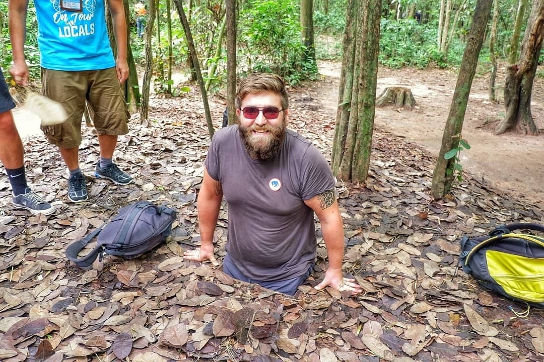 A person partially out of a small hole in a wooded area.