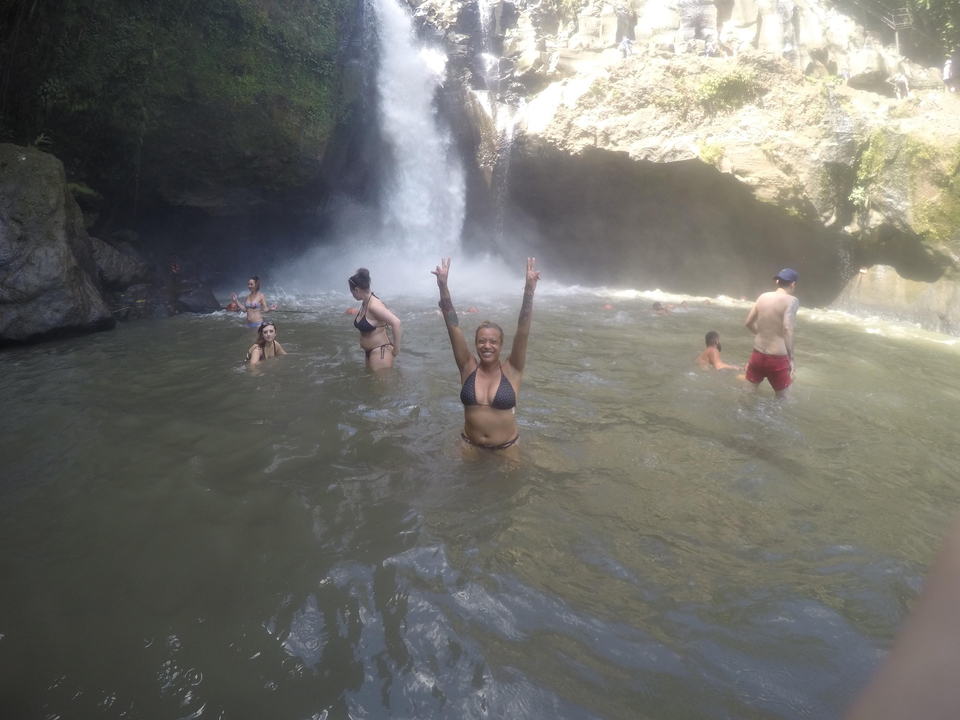 People swimming at the base of a waterfall.
