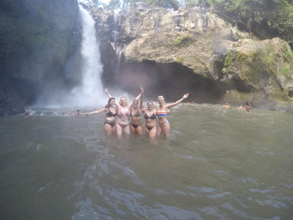 Group of friends swimming in front of a waterfall.