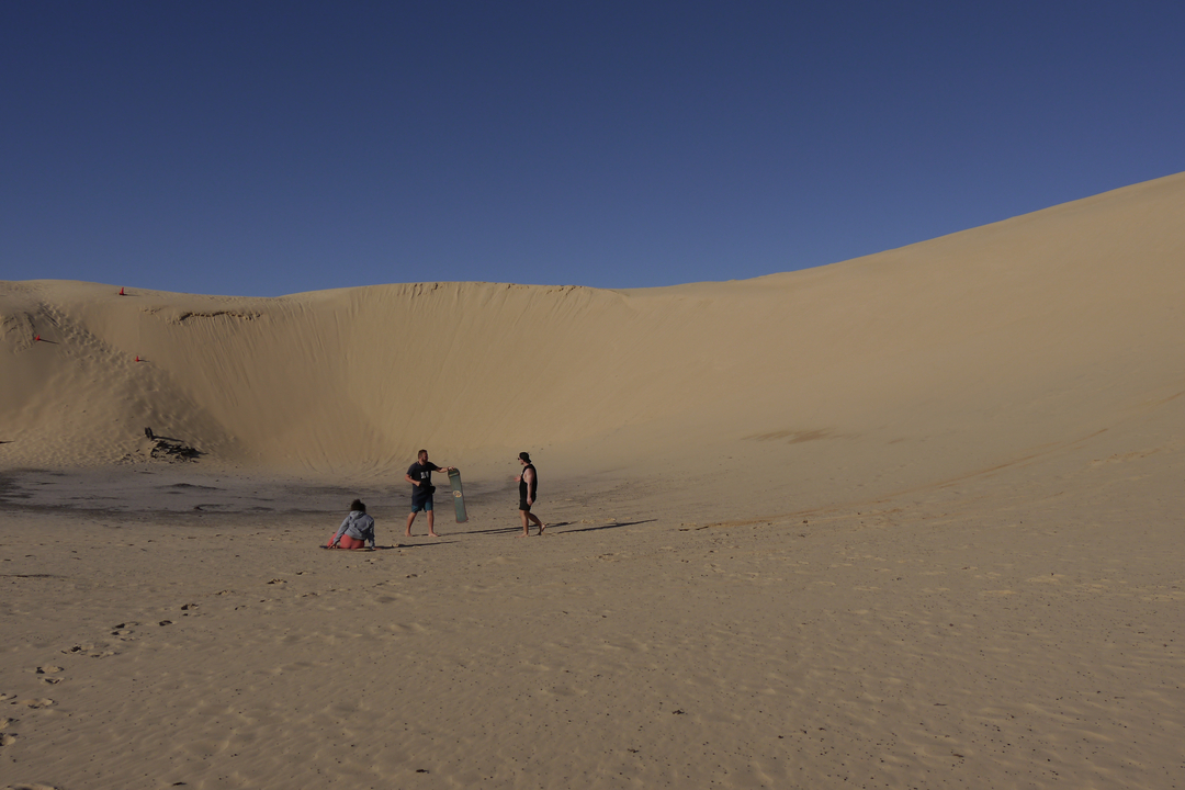 People on sand dunes, with one sitting on the slope.