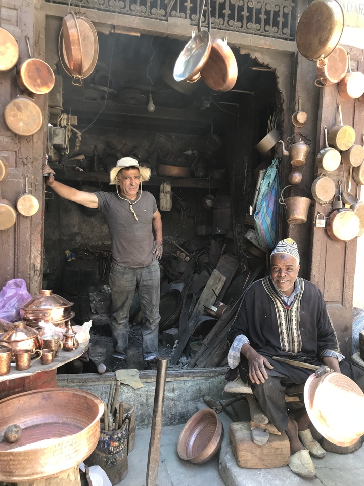 Two men posing in front of a shop with copper items.