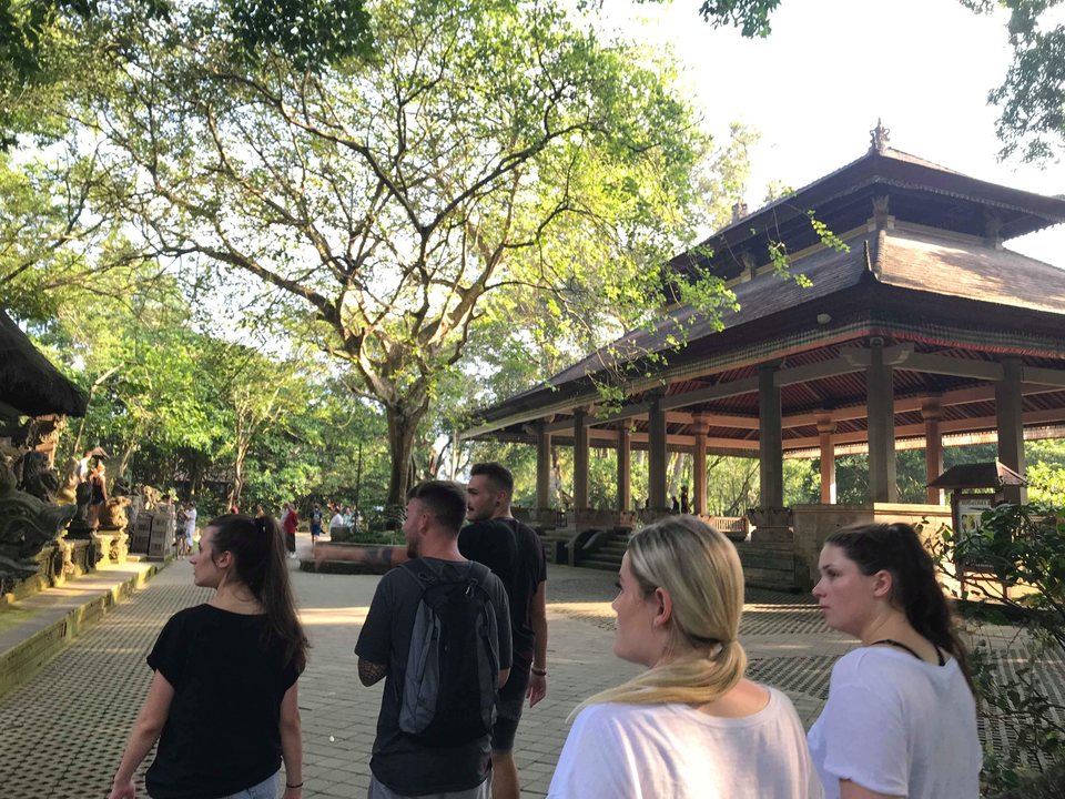 Group of people walking near a traditional building in a lush area.