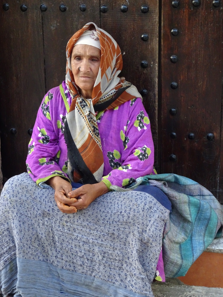 Woman in traditional clothing sitting in front of a wooden door.