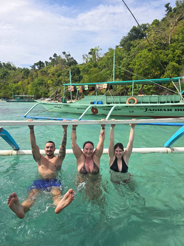 People swimming and posing behind a boat.