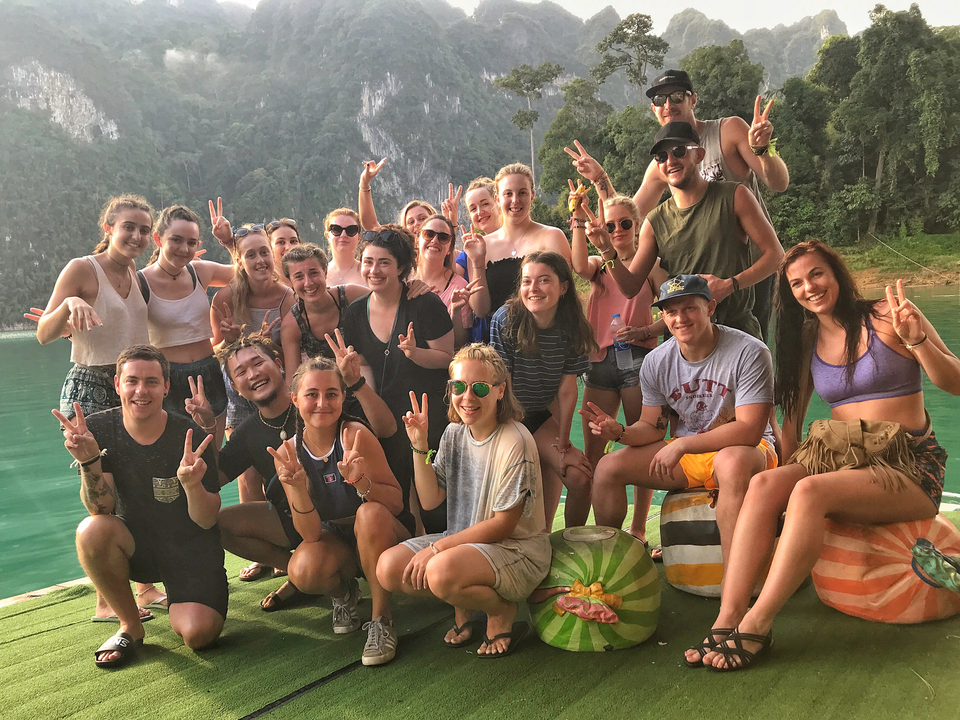 A group of friends posing in front of a lake with a mountainous backdrop.