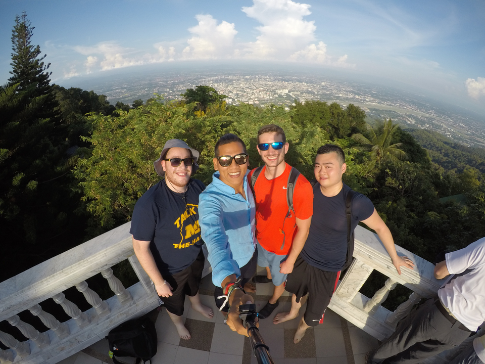 Four friends taking a selfie on a viewpoint overlooking a city and forest.