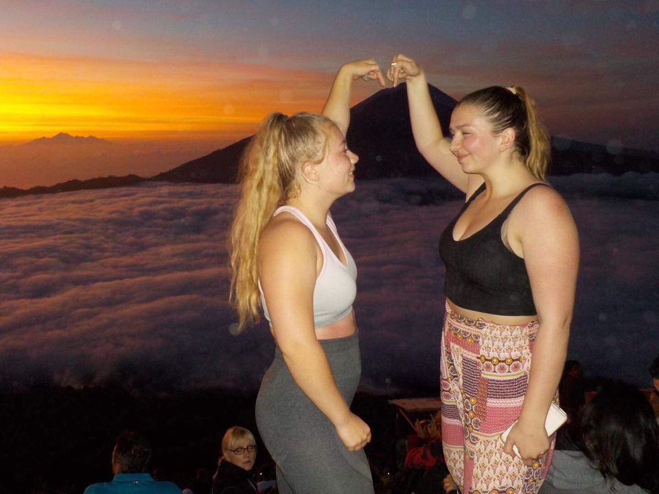 Two people posing with a scenic sunrise and a mountain in the background.