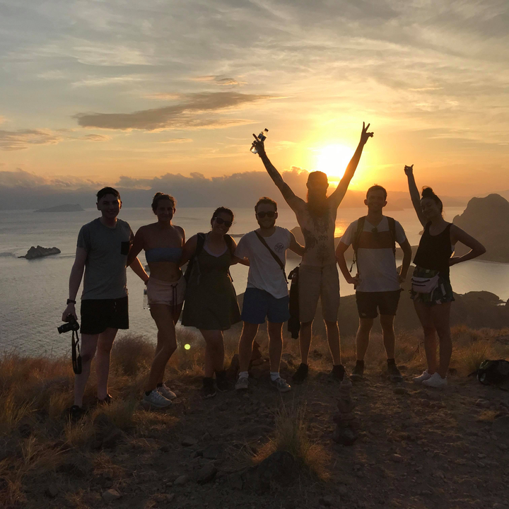 Group of people with raised hands enjoying sunset on a hill.