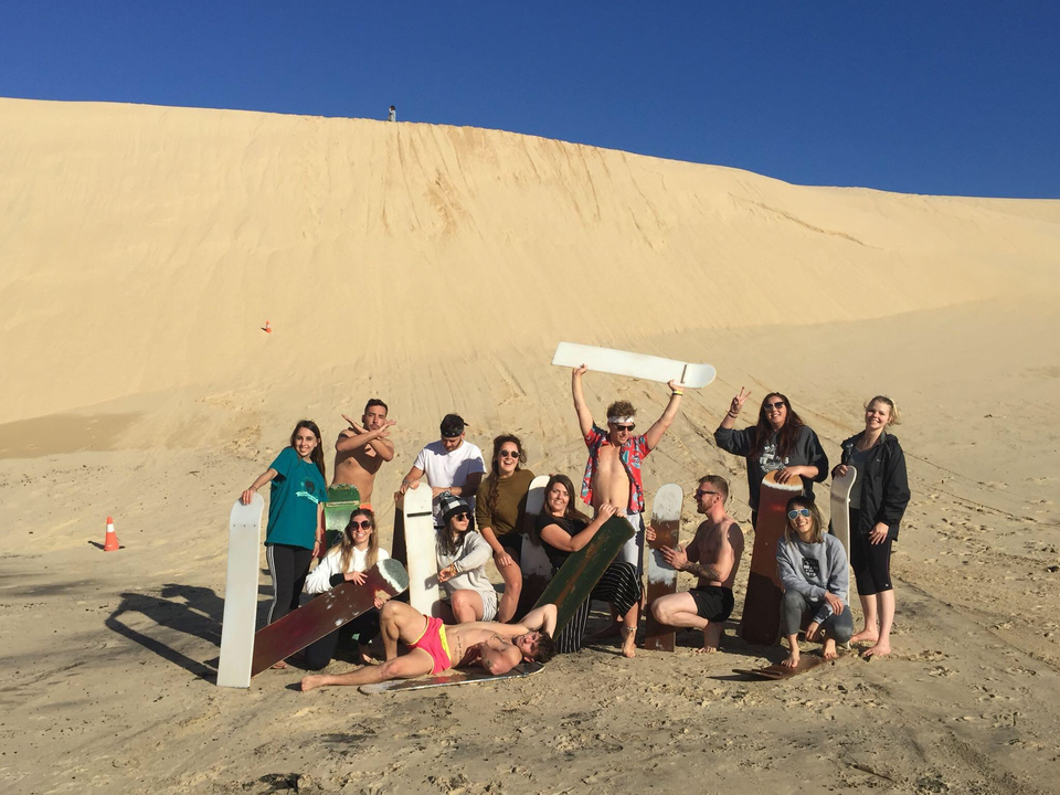 A group of people holding sandboards at the base of a dune.