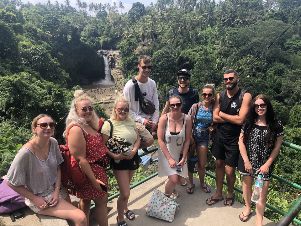 Group of people posing in front of a waterfall and lush vegetation.