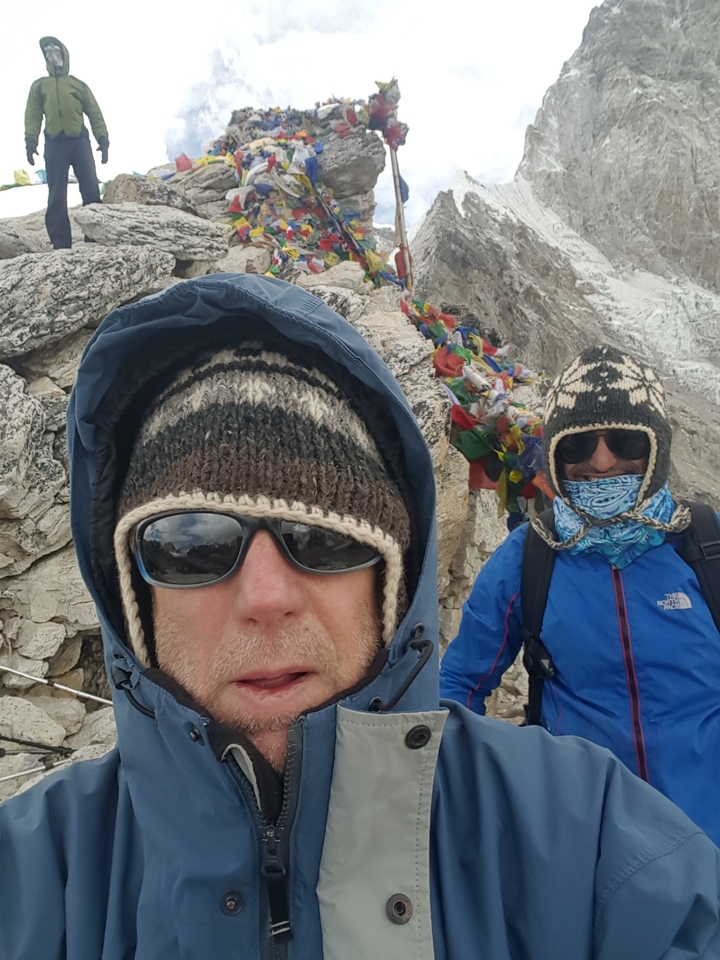 Two people in warm clothing with prayer flags and a mountainous landscape.