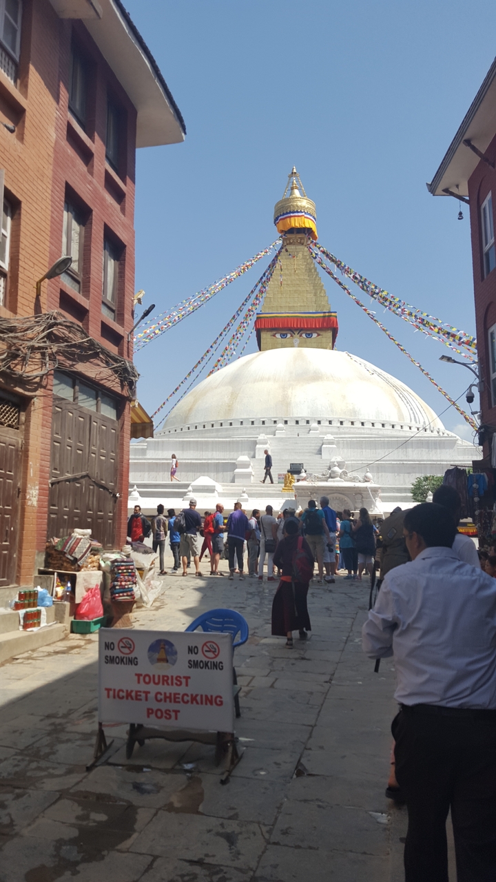 People gathered in front of a large, white stupa with eye symbol.