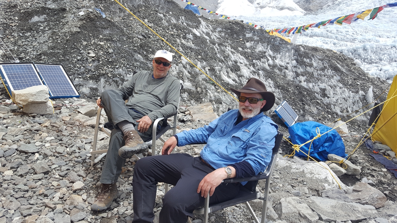 Two men sitting on chairs in a rocky area with visible solar panels.