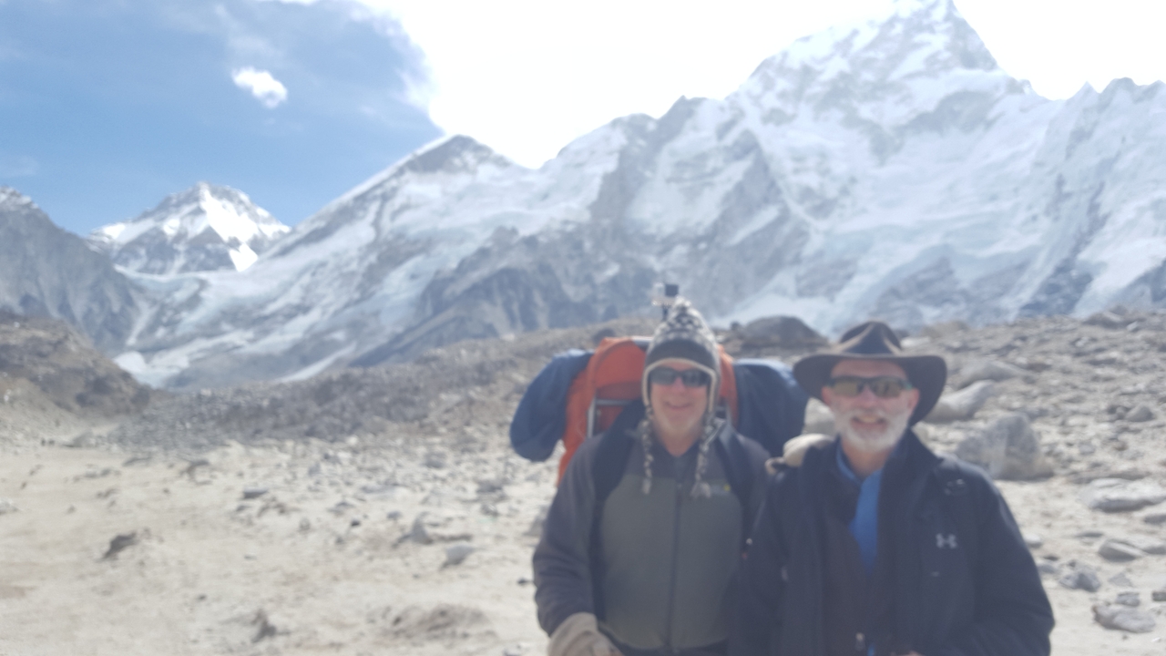 Blurred image of two people with backpacks against a mountainous backdrop.