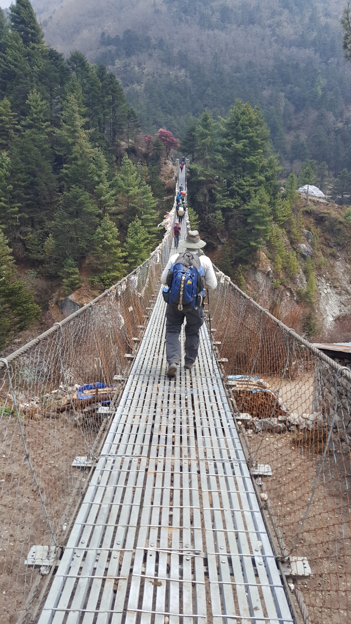 Person crossing a suspension bridge in a mountainous area.