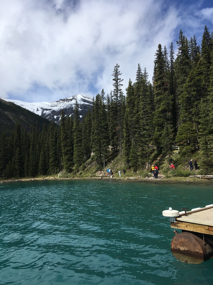 People by a clear turquoise lake with mountain backdrop
