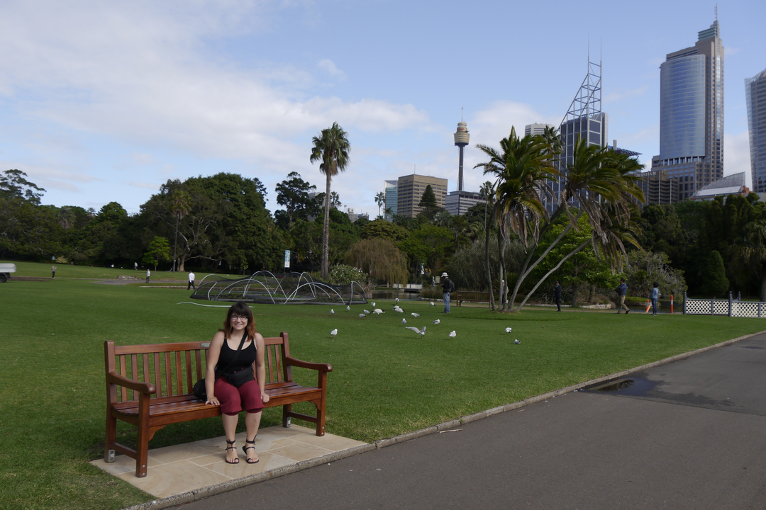 A person sitting on a bench in a green park with city buildings in the background.