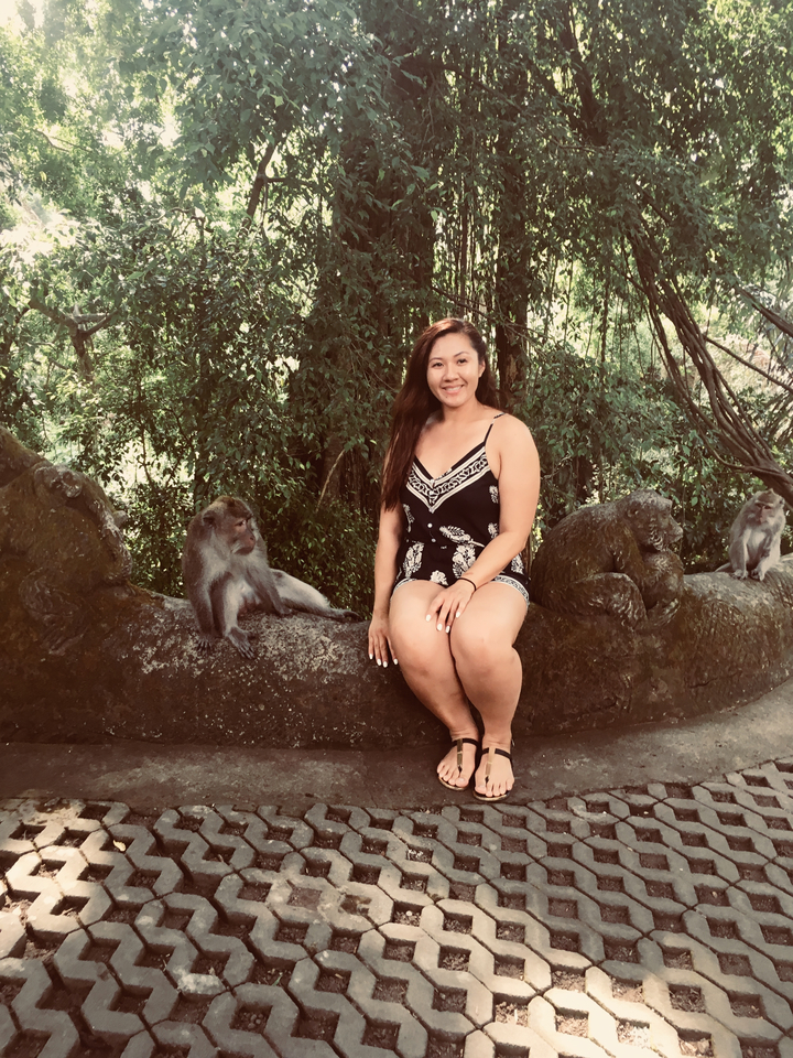 Woman sitting on a stone bench with monkeys around.