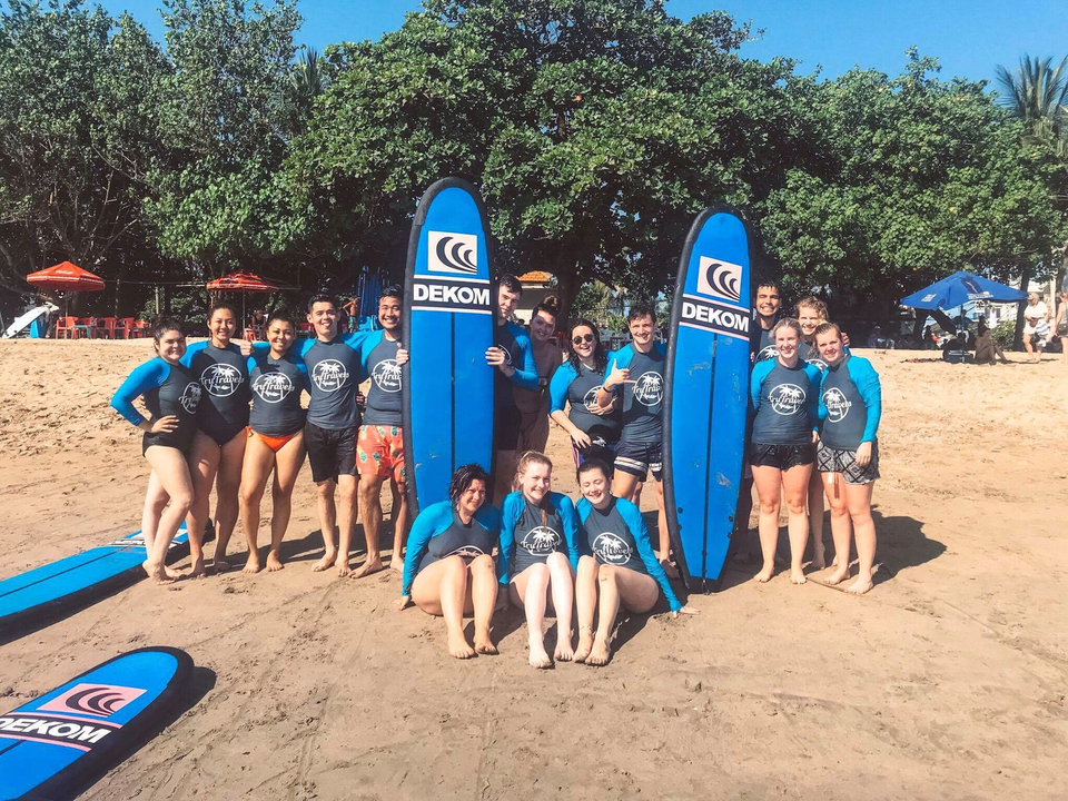 Group of people in matching surf outfits posing on a beach with surfboards.