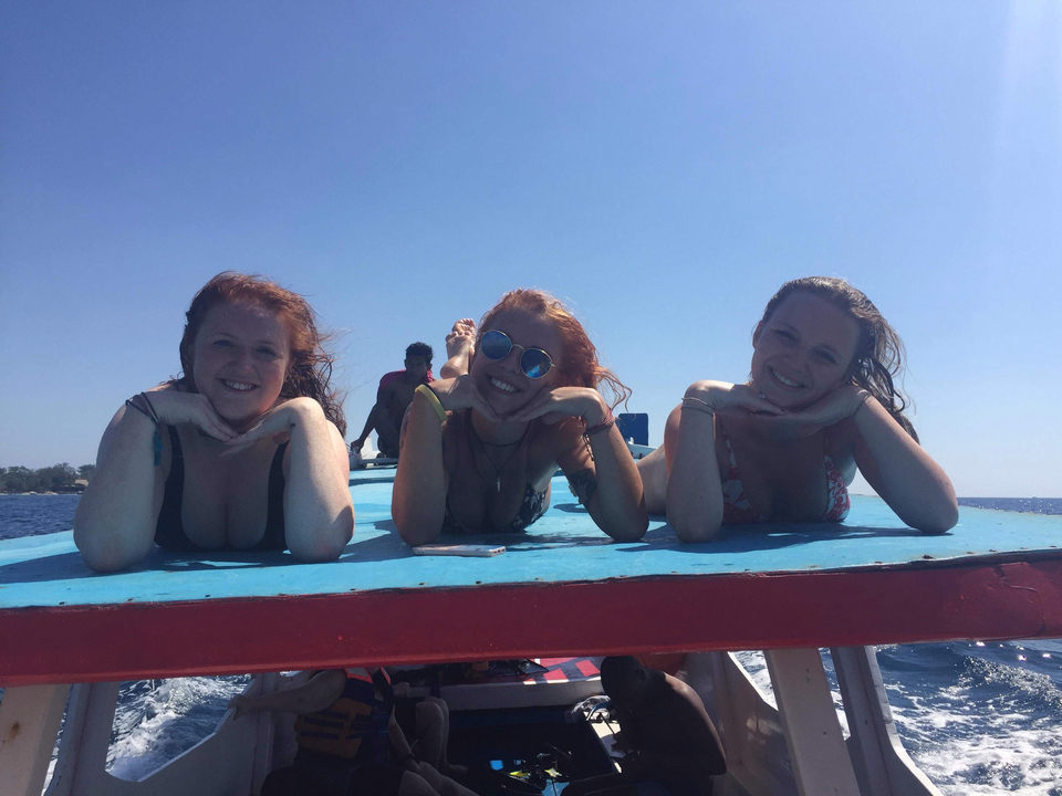 Three friends laying on a boat deck smiling with the ocean in the background.