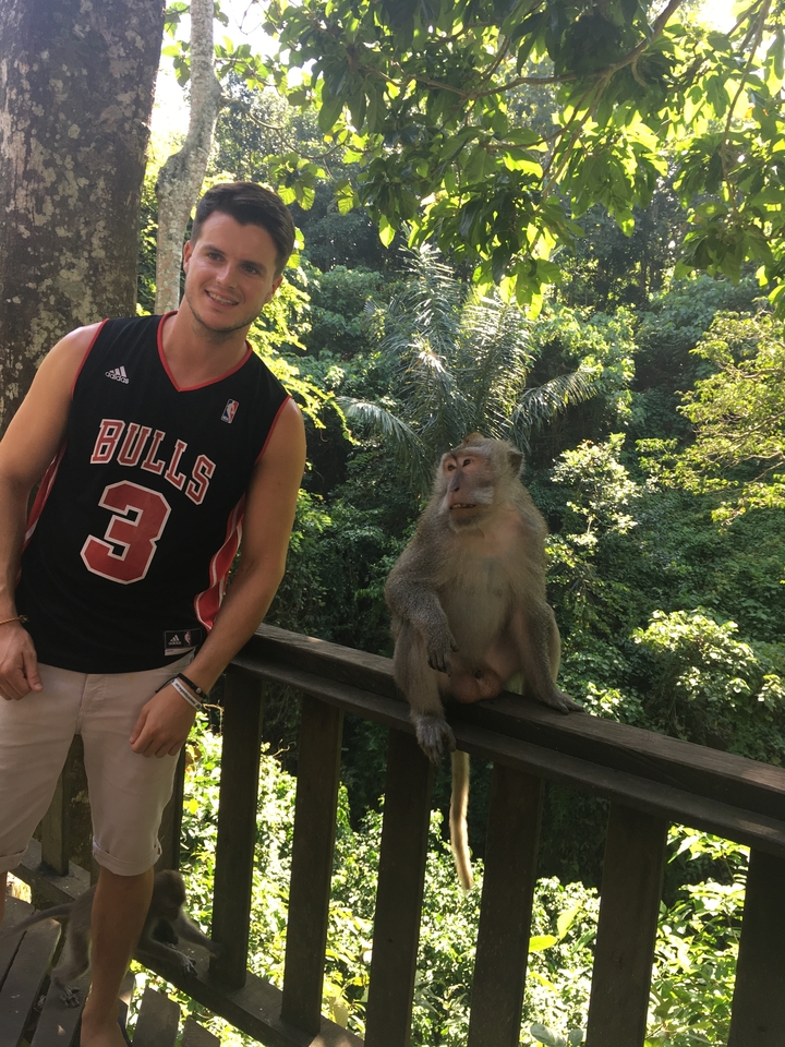 Man posing with a monkey sitting on a railing in a lush environment.