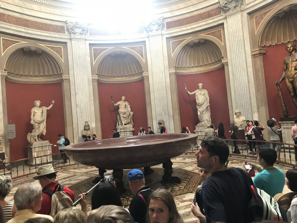Large ancient bowl surrounded by statues with visitors.