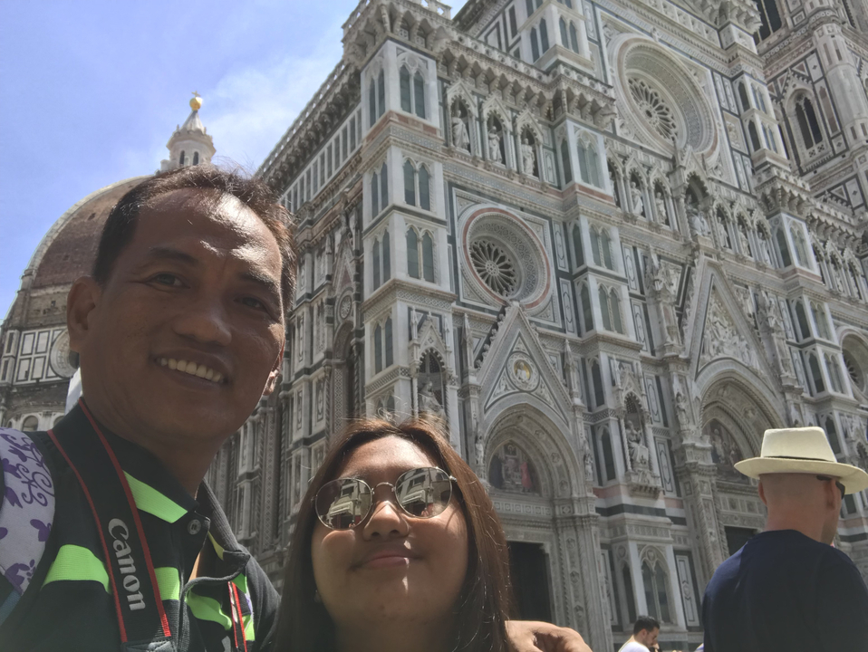 Two people smiling in front of a large cathedral with a dome.