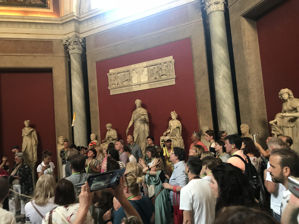 Museum hall with large statues and a crowd of visitors.