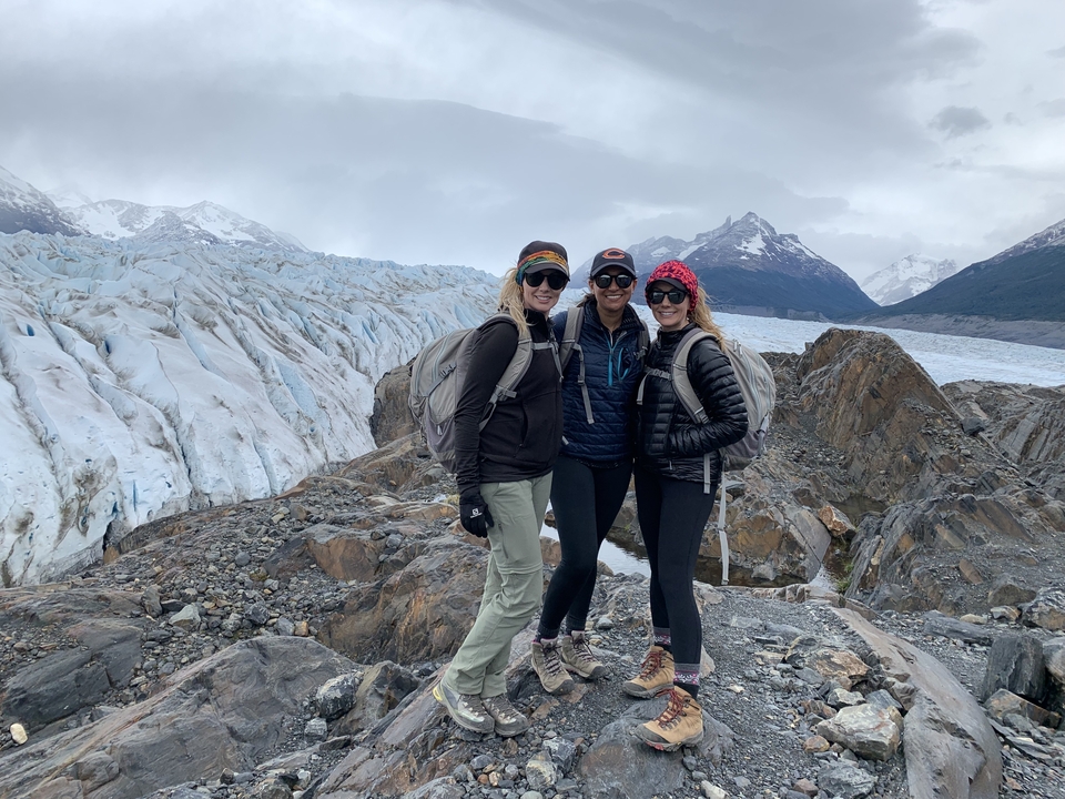 Three people posing on a rocky area in front of a glacier.