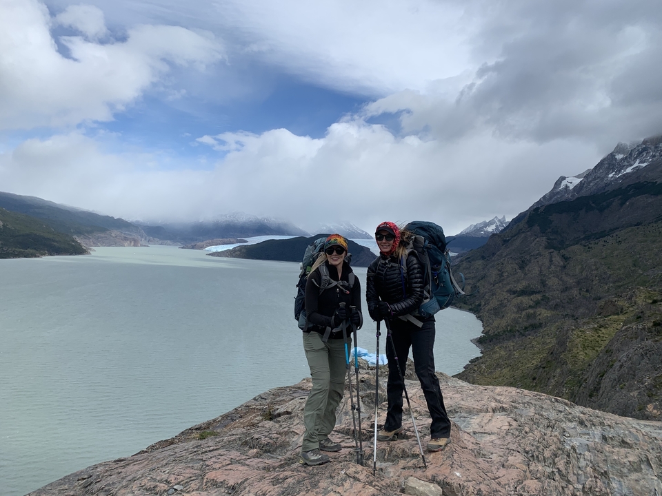 Two people standing on a cliff overlooking a glacier.