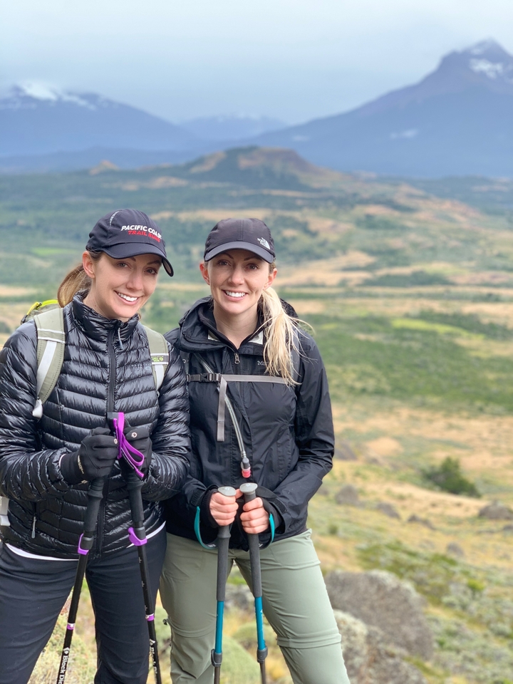 Two people in outdoor gear with a scenic landscape behind them.