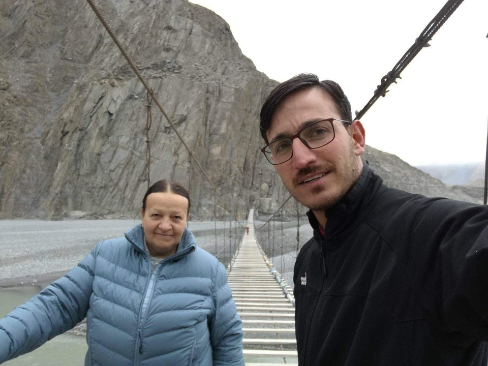 Two people posing on a suspension bridge over rocky terrain.