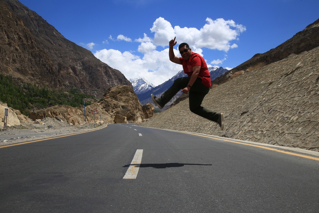 Person jumping on a road with rugged mountains.