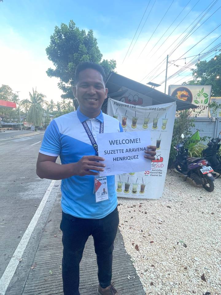 Person holding a welcome sign with a background of a street and poster.