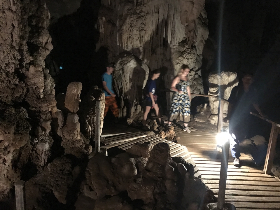 People exploring a dark cave with stalactites.