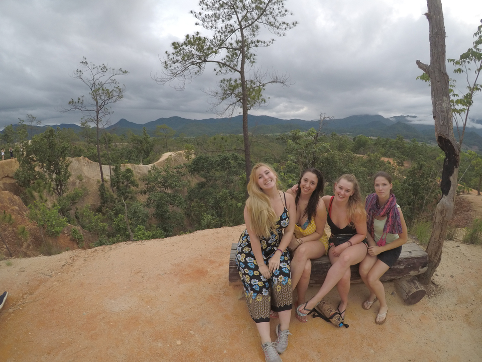 Four women sitting on a bench overlooking a scenic view.