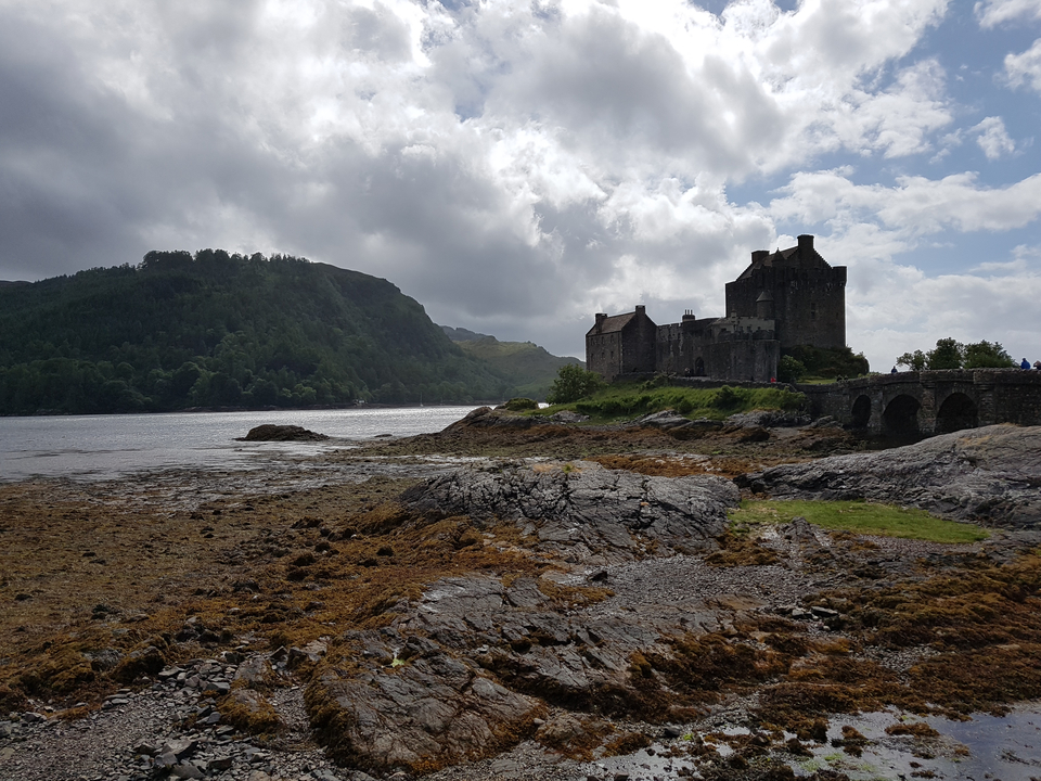 A castle by the water with cloudy skies.