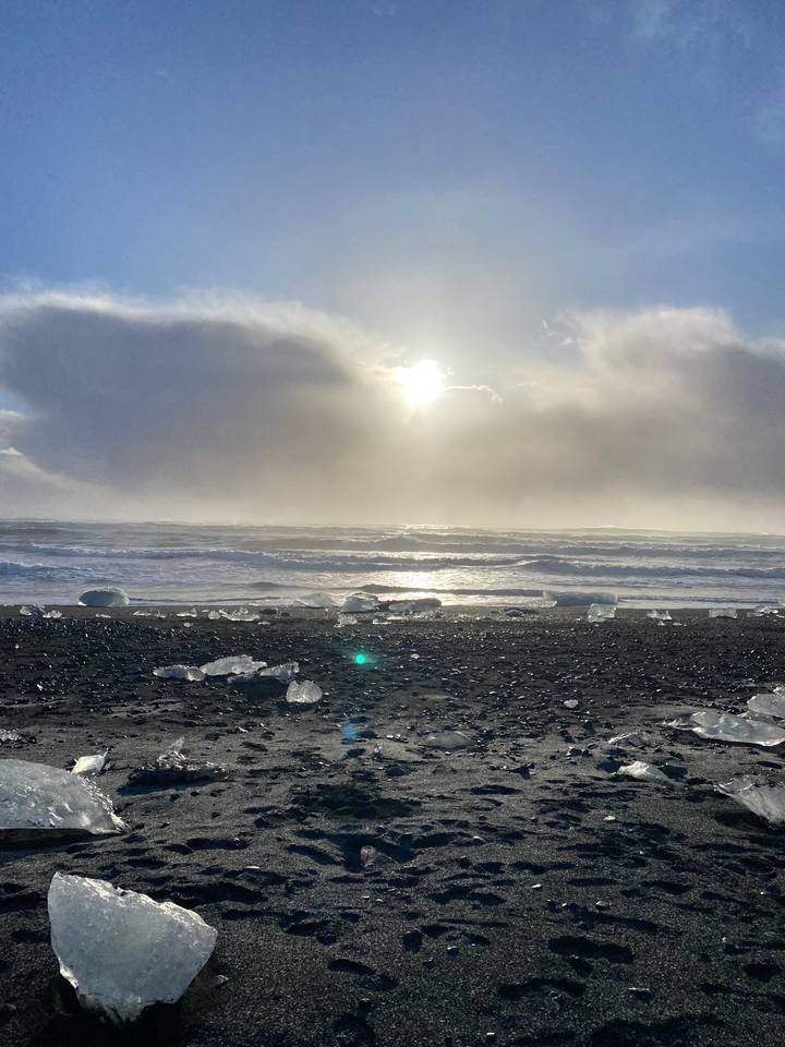 Black sand beach with sunlight and ice fragments.
