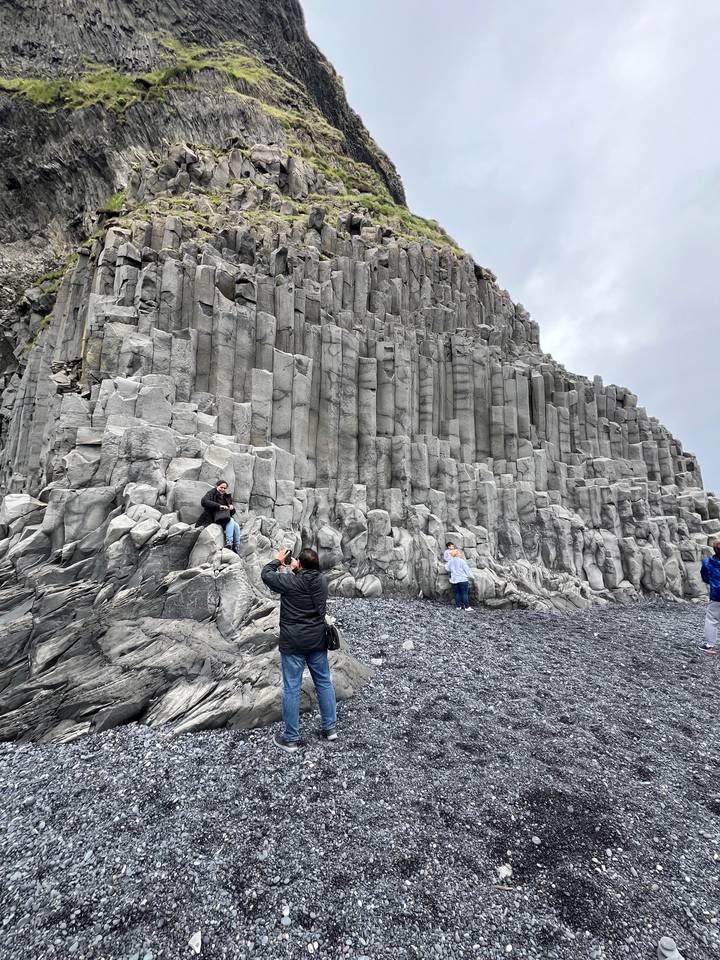 Tourists exploring basalt columns at a volcanic beach.