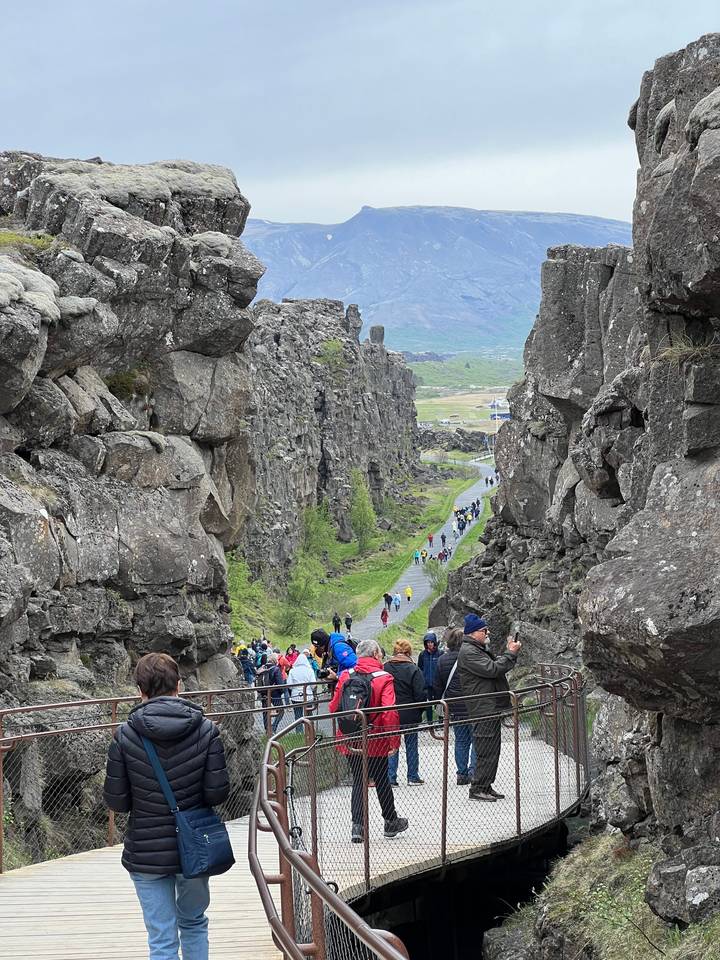 Visitors walking through a rocky landscape with dramatic cliffs.